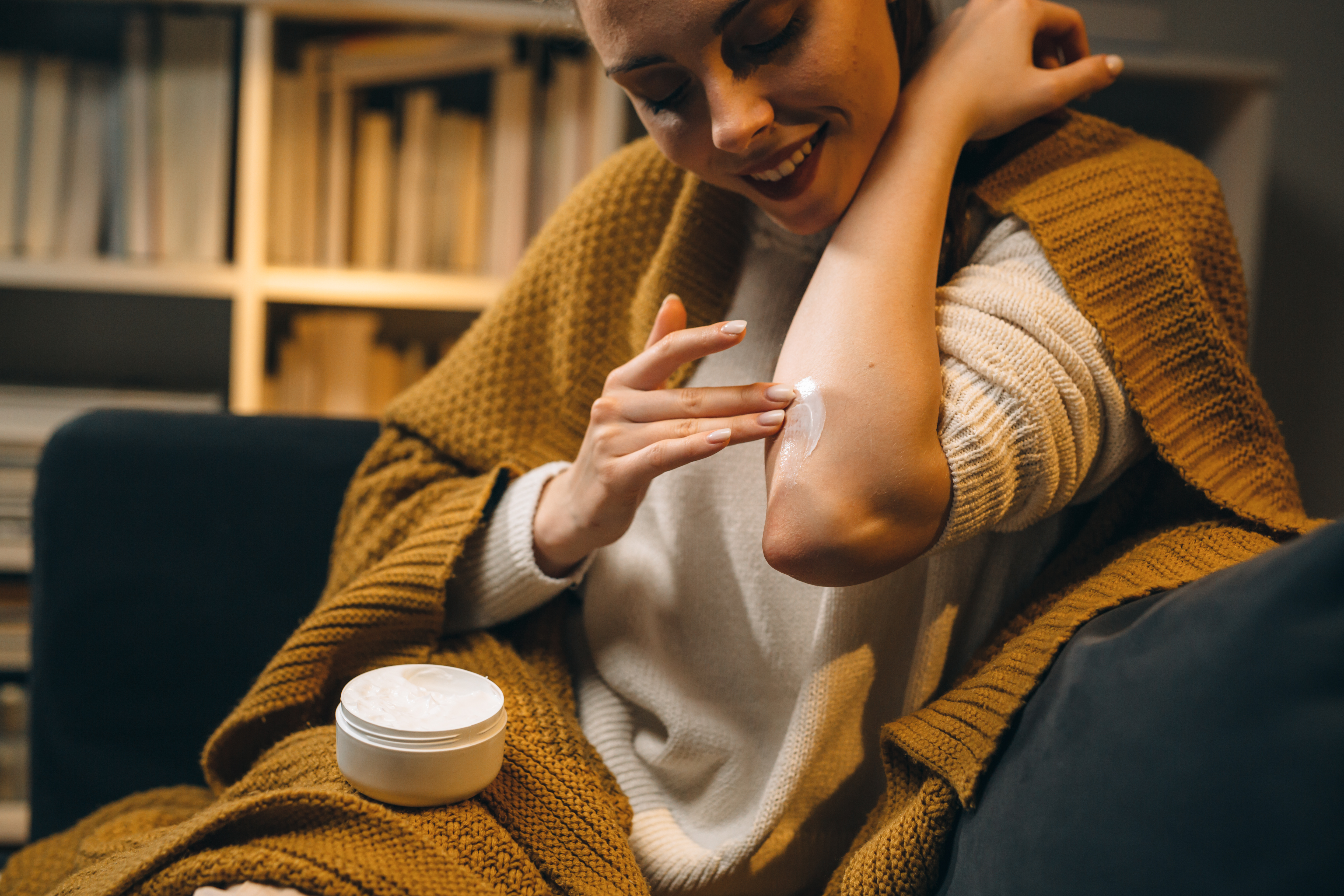 Woman applying moisturizer to her elbow while sitting on a couch